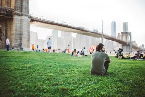 Man sitting on gree surface, enjoying the view of the Brooklyn Bridge after long distance moving companies New York City have helped him settle in.