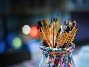 A color-stained cup, filled with painting brushes.