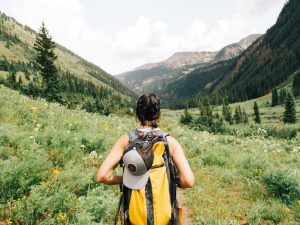 A woman hiking through mountains with a yellow backpack.