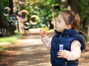 A small girl blowing soap bubbles in a park.