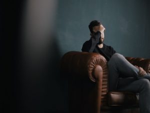 A man sitting on a brown leather sofa, thinking about homesickness.