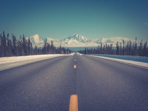 A road in Alaska, stretching towards snowy mountains.