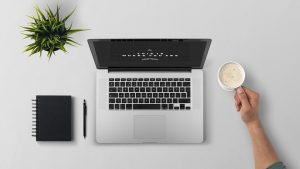 Laptop on a desk along with a cup of coffee, plant and a planner.