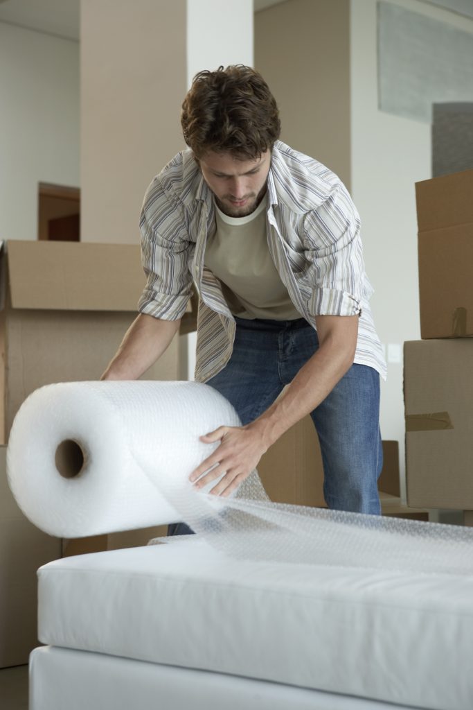 Man wrapping a bed with bubble wrap as one of the cross country moving companies Nampa professionals 