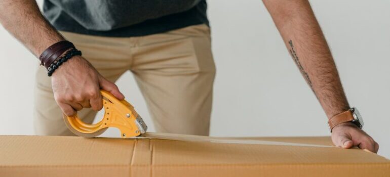 man sealing cardboard box with tape