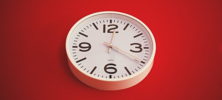 A white clock on a red background, representing time you could lose looking for the best cross country movers West Des Moines has.