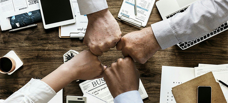 Four people bumping fists over their working desk