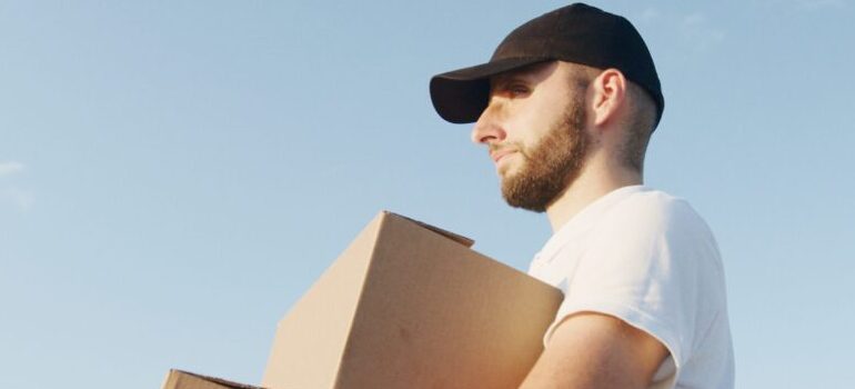 man in a white shirt and black hat carrying moving boxes