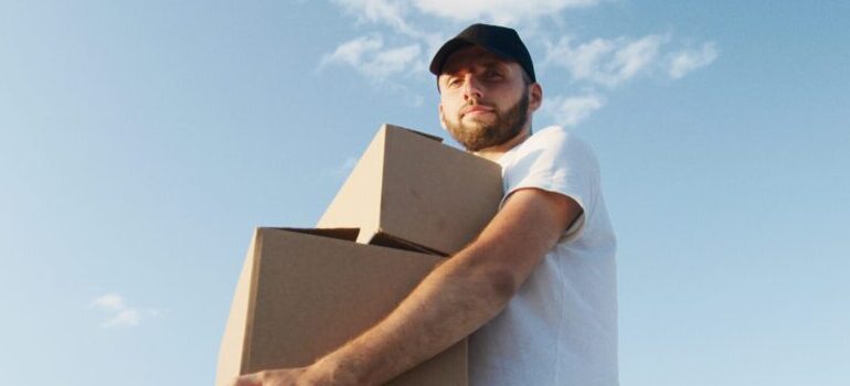 male in a white shirt with a black had carrying moving boxes