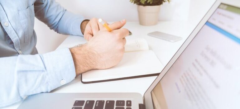 a person writing into a notebook with laptop by their side