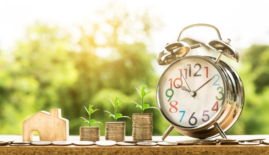 A wooden model of a home, three stacks of coins, and a clock