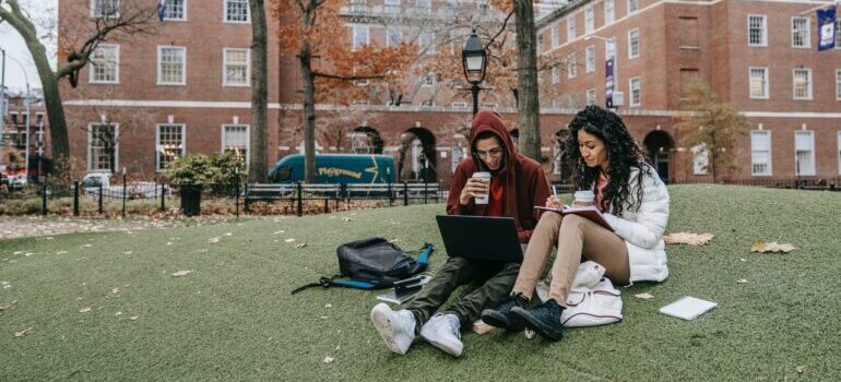 Two students studying on a lawn in front of the university buuilding.
