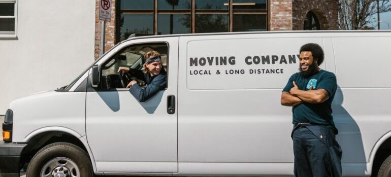 A moving worker stands next to a moving van