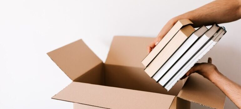 Person holding books and putting them into a cardboard box.