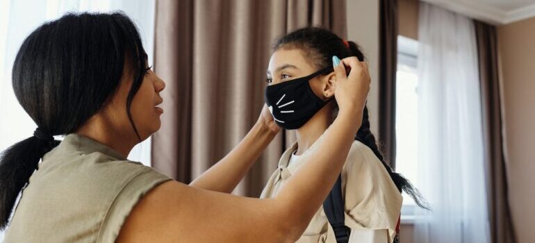 A mother putting a face mask on her daughter.