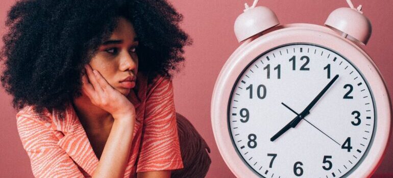A bored woman looking at a large clock.