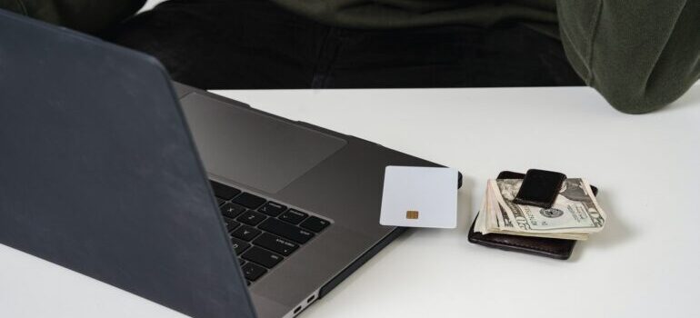 A stack of money, a credit card, and a laptop on a table.