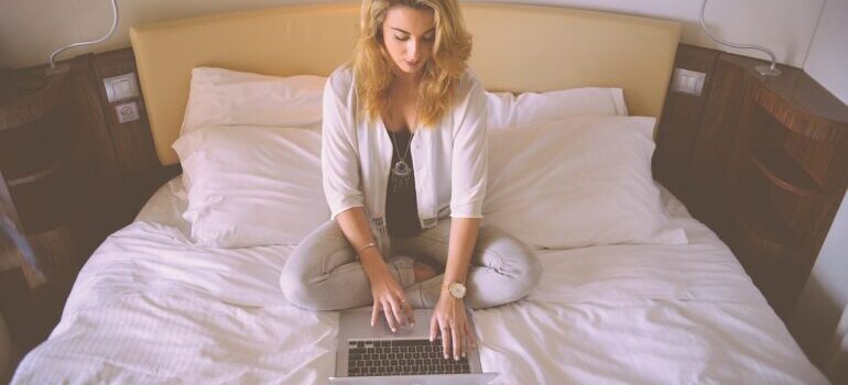 A woman sitting on a bed, searching for long distance movers Las Vegas on a laptop.