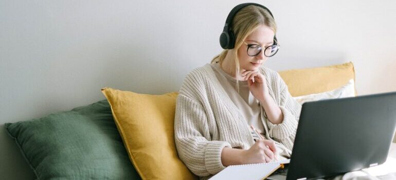 A woman with glassess and headphones using laptop to research the traits of a reputable moving company.