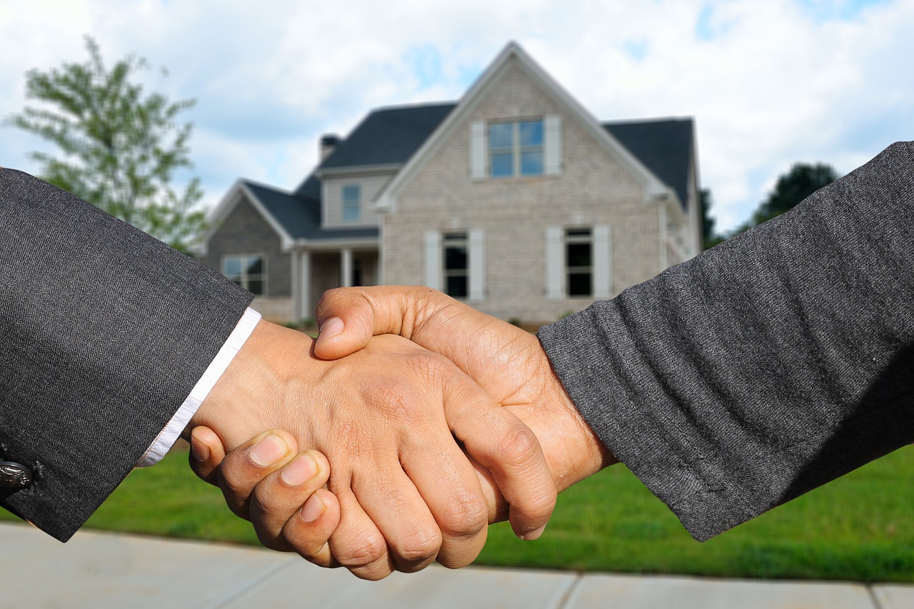 two men in suits shaking hands in front of a house