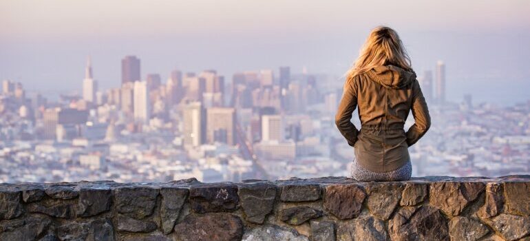 A woman sitting on a ledge, looking at San Francisco.