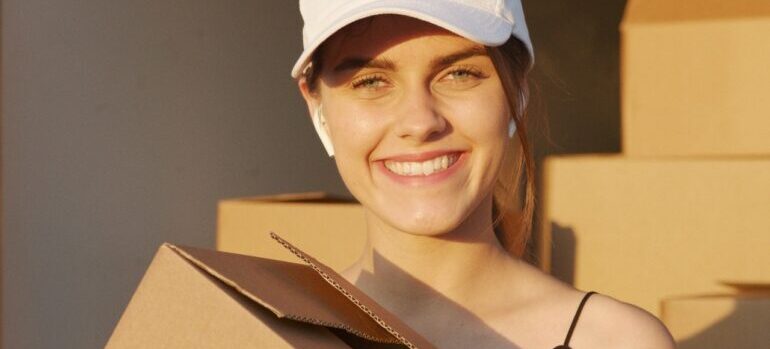A woman smiling and holding a moving box.