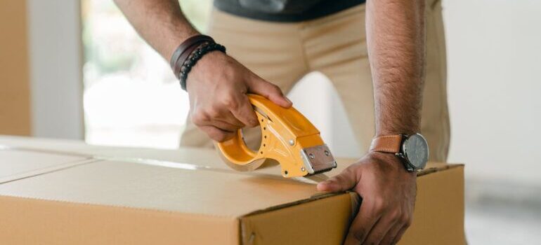 A person sealing a moving box with a tape as representative of A2B Movers 