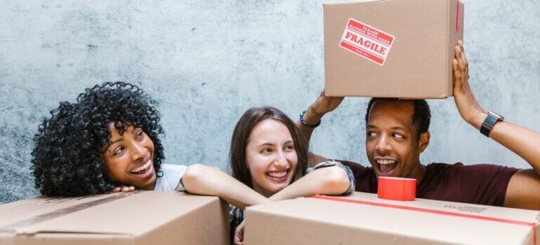three smiling people leaning on moving boxes