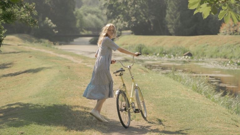 A woman pushing a bike in nature.