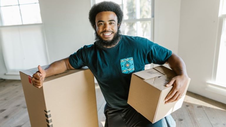 A mover smiling and holding moving boxes.