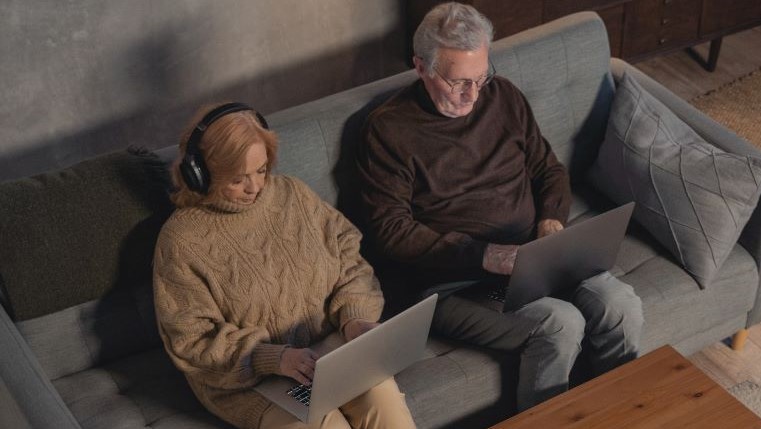 Elderly couple researching on laptops.