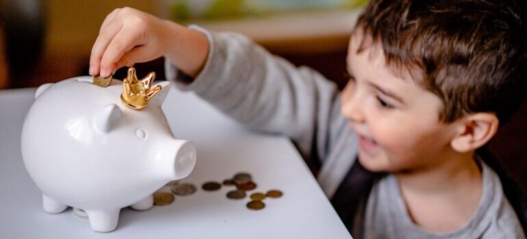 A boy putting coins in a white piggy bank.