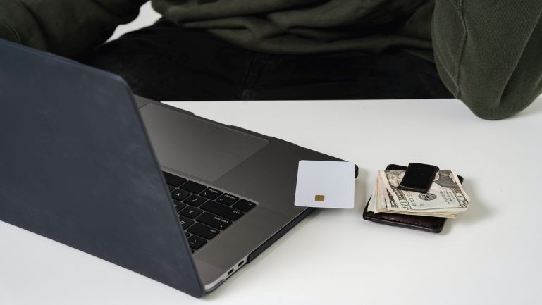 Money, debit card, and a laptop on a desk.