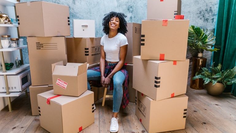 A woman sitting amoing moving boxes.