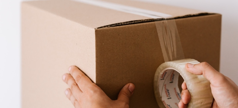 A person sealing moving box as a symbol of long distance movers Ashburn that provide packing services 
