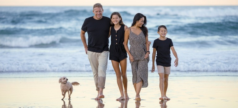 A family of four walking down the beach with a dog.