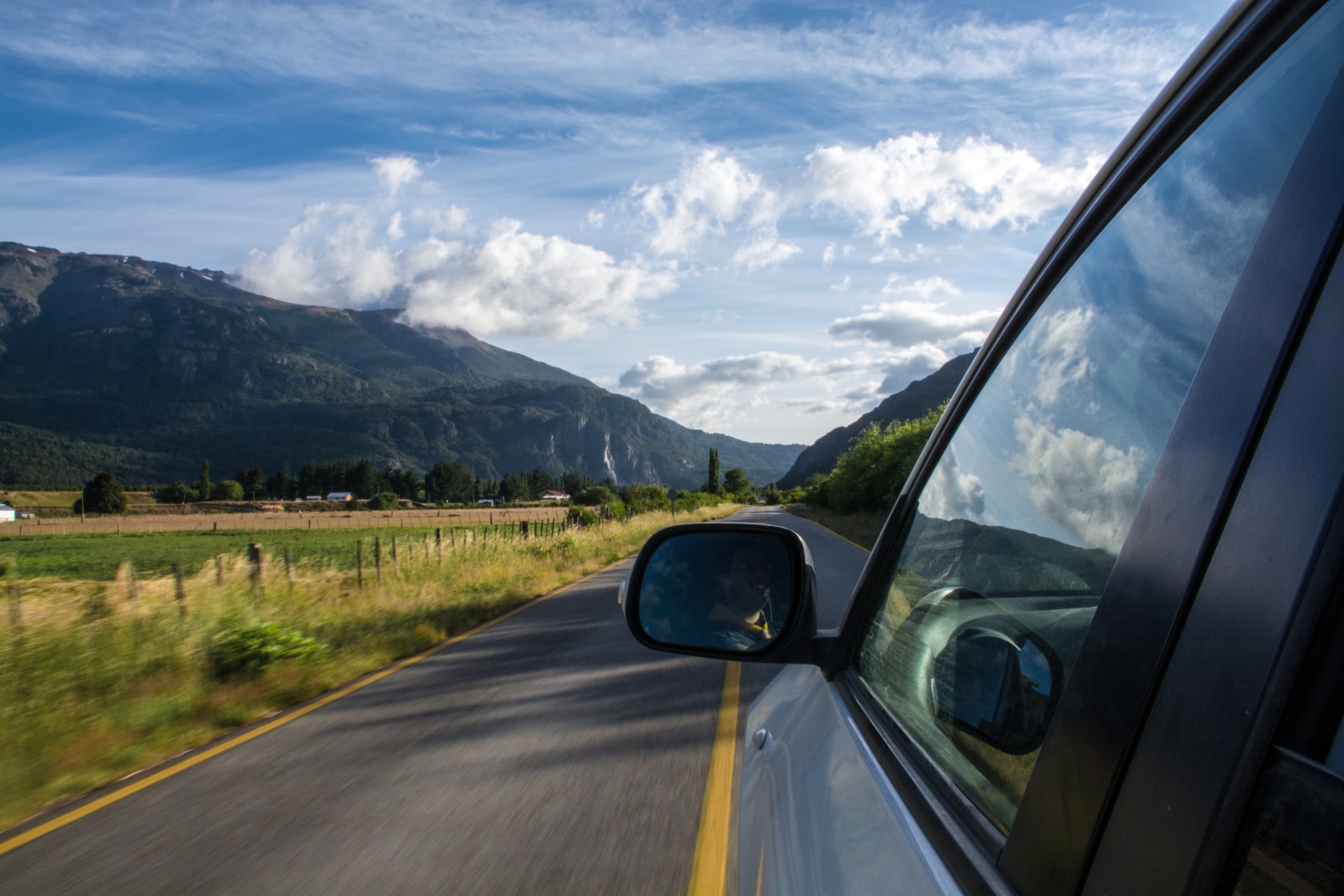 a car on the road with mountains and green pastures ahead