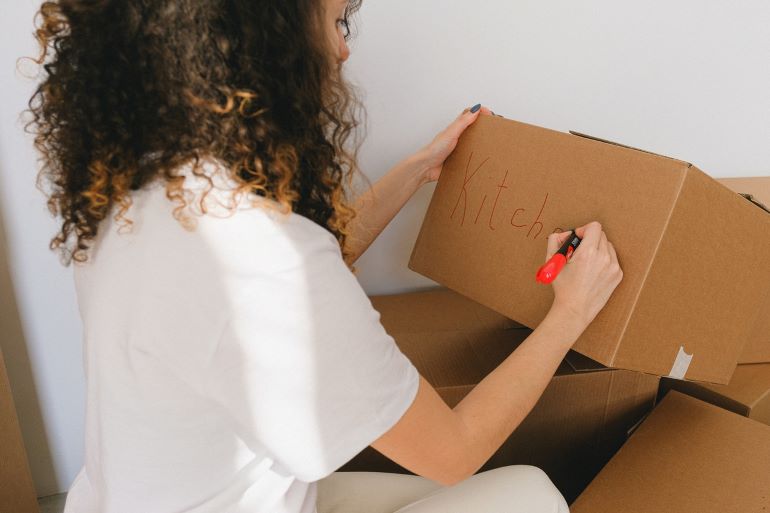 a woman writing the word kitchen on a cardboard box