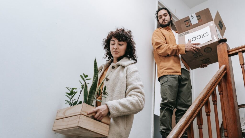 a woman and a man carrying boxes and flowers down the stairs