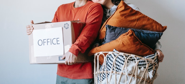 A couple holding moving box and pillows 