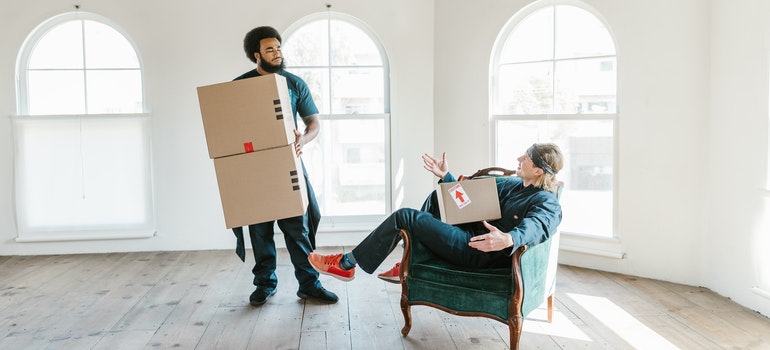 Two men from long distance moving companies Pembroke Pines chatting with carton boxes in their hands.
