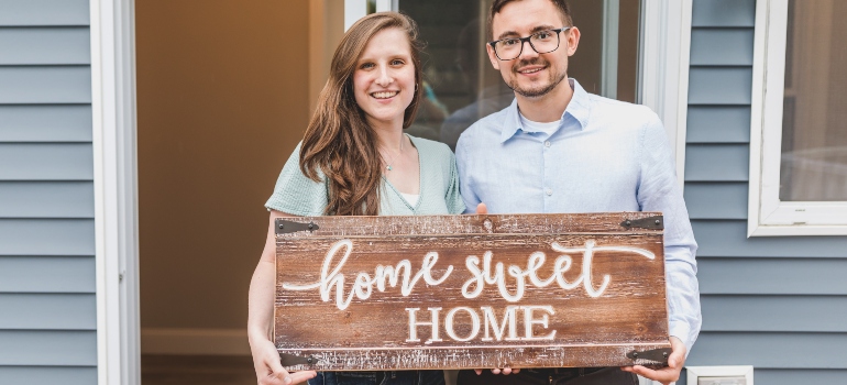 A man and a woman holding a sign in front of their new house