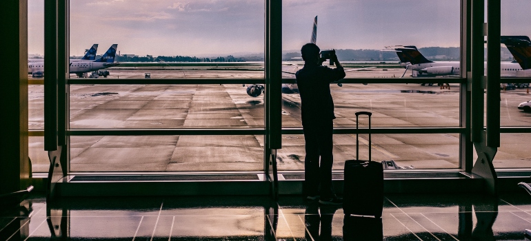 A man with a suitcase photographing planes at the airport.