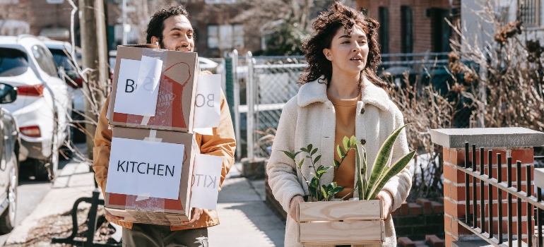 A man carrying two boxes with a woman next to him who is carrying a plant.