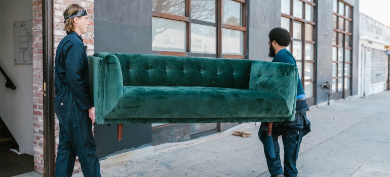 Two workers from top movers in Raleigh carrying a couch in the street.