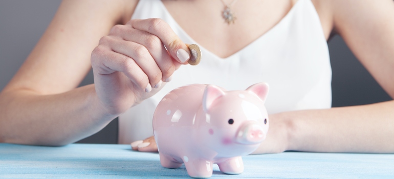 A woman putting a coin in the piggy bank.