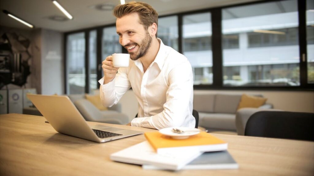 A man smiling and drinking coffe at work.