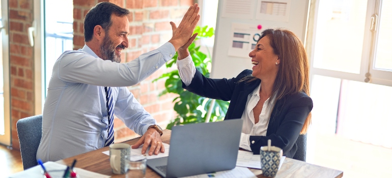 A man and a woman giving each other a high five in the office.