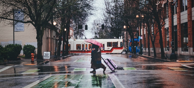 A person with pink umbrella strolling their luggage on the street.