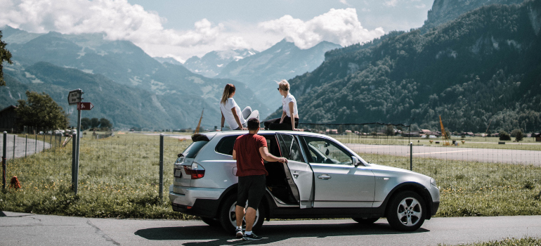 A group of friends with their car looking at natural scenery.